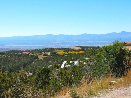 A scenic view of rolling hills and mountains under a clear blue sky, with patches of trees and distant yellow foliage.