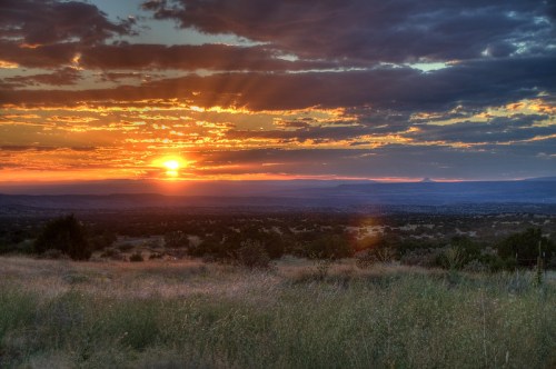 A vibrant sunset over a vast landscape, with colorful clouds and rays of light illuminating the horizon.