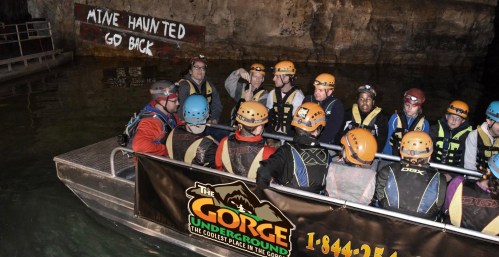 A group of people in helmets on a boat inside a dark underground mine, with a "Mine Haunted" sign in the background.