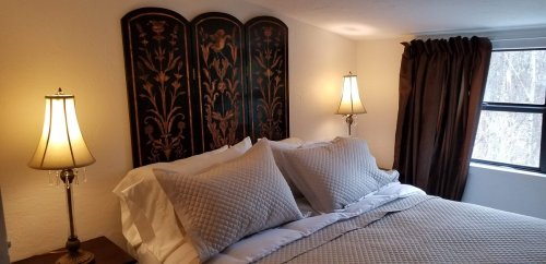 Cozy bedroom with a decorative headboard, two lamps, and a large window with curtains.
