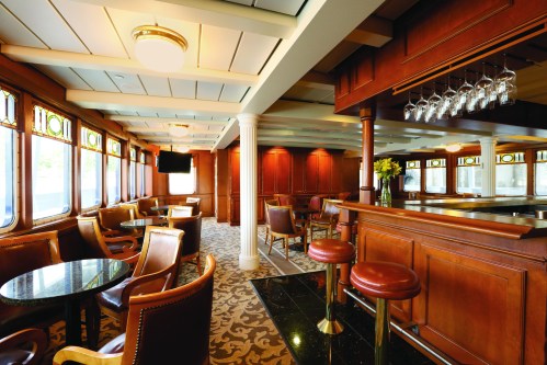 Elegant lounge with wooden decor, bar area, and large windows, featuring plush seating and a cozy atmosphere.