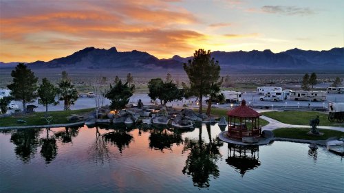 Scenic sunset over mountains, reflecting in a calm pond with a gazebo and RVs in the background.