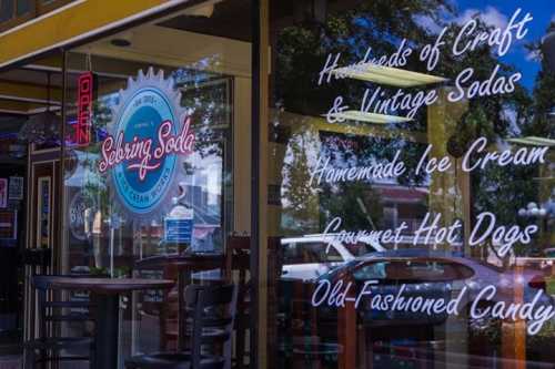 A storefront window displaying a sign for a soda shop with ice cream, hot dogs, and vintage candy offerings.