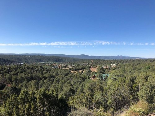 A panoramic view of a green landscape with hills and a clear blue sky, dotted with small buildings in the distance.