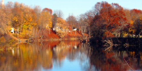 A serene river scene surrounded by vibrant autumn foliage reflecting on the water's surface.