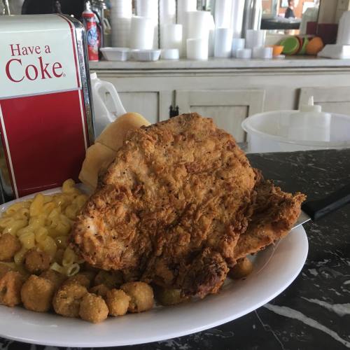 A plate of fried chicken, macaroni and cheese, and a side of hushpuppies, with a Coke can in the background.