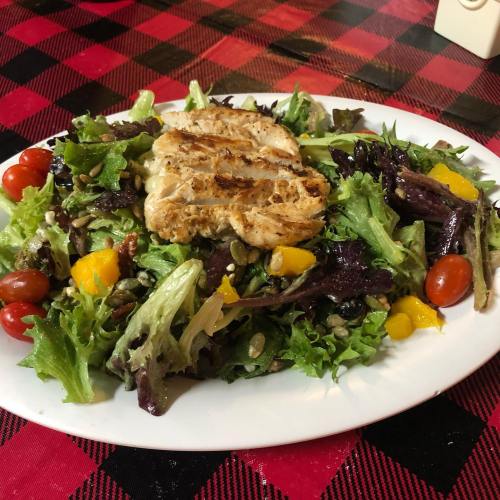 A colorful salad with grilled chicken, mixed greens, cherry tomatoes, and yellow peppers on a white plate.