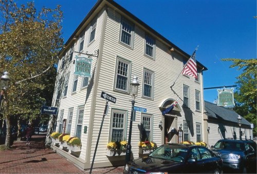 A historic building with a sign reading "Warwick Tavern," featuring an American flag and flower planters outside.