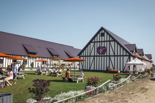 A charming outdoor venue with picnic tables, orange umbrellas, and a large, stylish building in a sunny setting.
