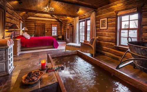 Cozy log cabin interior featuring a bedroom, a wooden soaking tub, and warm lighting.