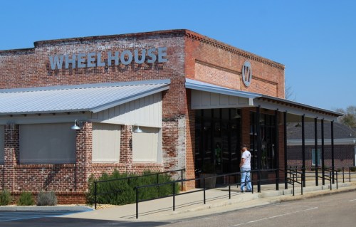 Exterior of a brick building with the sign "WHEELHOUSE," featuring a ramp and a person standing outside.