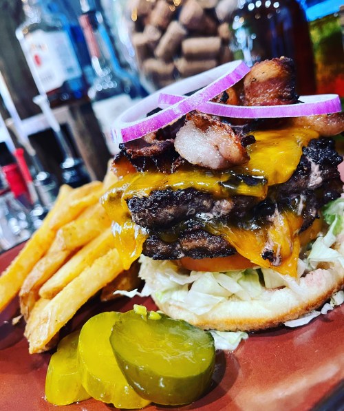 A juicy cheeseburger with bacon, lettuce, tomato, and pickles, served with crispy fries on a plate.