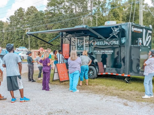 A food truck named "Wheelhouse" with a line of people waiting to order in a grassy area.