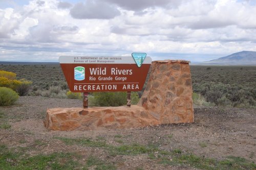 Sign for Wild Rivers Recreation Area at Rio Grande Gorge, featuring a stone base and scenic landscape in the background.