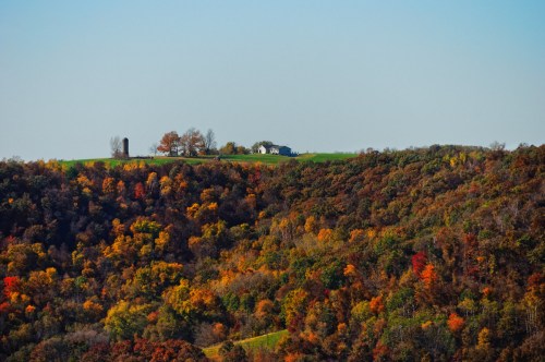 A scenic view of rolling hills covered in vibrant autumn foliage, with a farmhouse on a distant hilltop.