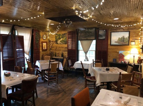 Cozy restaurant interior with wooden walls, tables set for dining, and warm lighting from string lights and lamps.