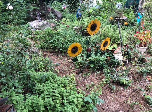 A garden scene with vibrant sunflowers among lush greenery and decorative elements like rocks and small statues.