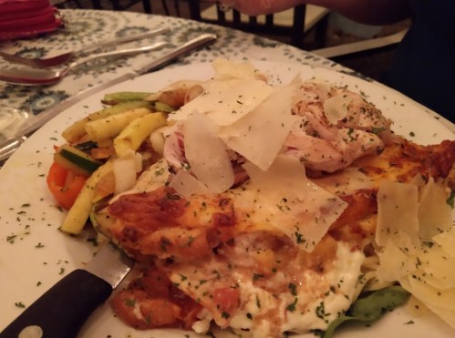 A plate of lasagna topped with cheese and herbs, accompanied by sautéed vegetables.