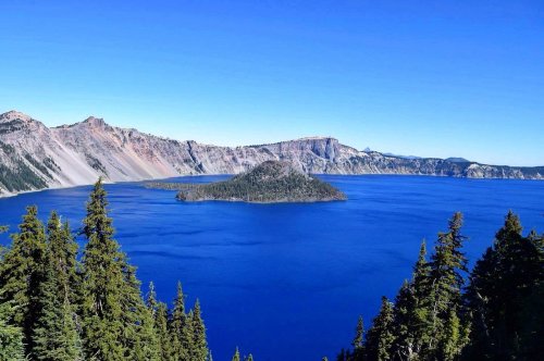 A stunning view of Crater Lake, featuring a deep blue lake and a small island surrounded by tall evergreen trees.