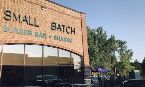 Exterior of Small Batch Burger Bar, featuring a brick facade and outdoor seating area under a clear blue sky.