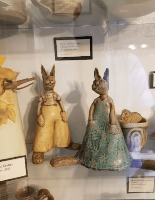 Two ceramic rabbit figurines, one in overalls and the other in a dress, displayed in a glass case.