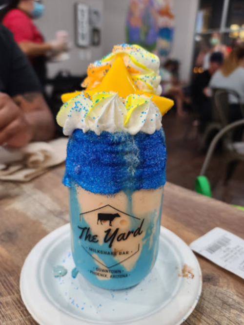A colorful milkshake topped with whipped cream, sprinkles, and a star-shaped decoration in a glass at a milkshake bar.