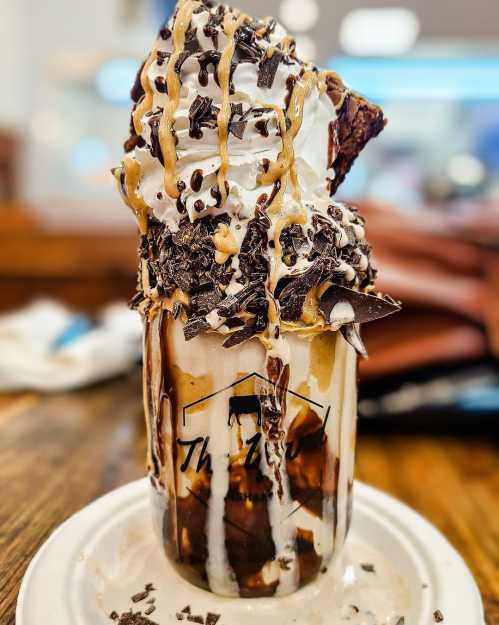 A decadent dessert in a glass, featuring whipped cream, chocolate shavings, brownie, and drizzled caramel.