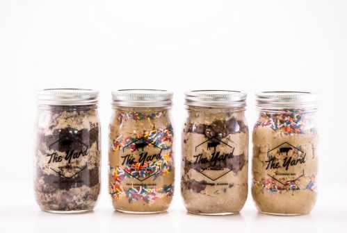 Four jars filled with layered desserts, featuring cookie dough, sprinkles, and chocolate, labeled "The Yard."