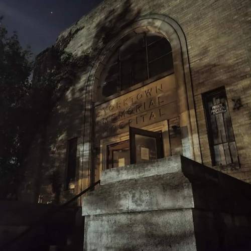 Dimly lit entrance of Yorktown Memorial Hospital, featuring a large arched doorway and stone steps. Shadows cast on the wall.