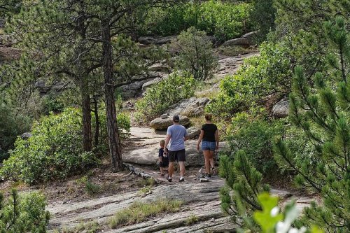 A family walks along a rocky trail surrounded by greenery in a natural setting.