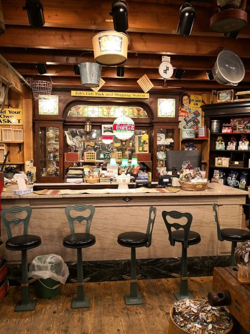 A vintage shop interior featuring a wooden counter, stools, and various nostalgic items and decor on the walls.