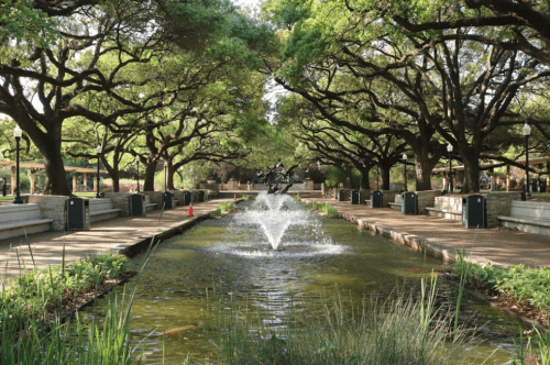 A serene park scene featuring a fountain in a pond, surrounded by lush trees and pathways.