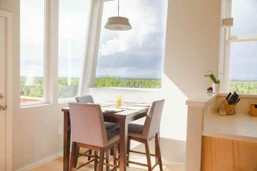 Bright dining area with a table and chairs, large windows showcasing a green landscape outside.