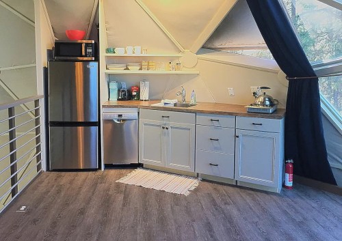 A modern kitchen in a geometric room, featuring stainless steel appliances, wooden countertops, and a large window.