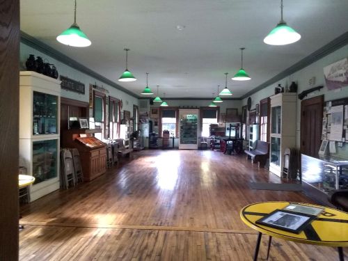 A spacious, well-lit room with wooden floors, green pendant lights, and display cases along the walls.