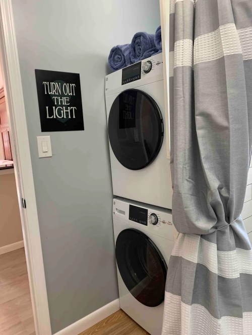 A laundry area featuring stacked washer and dryer units, with a sign that says "TURN OUT THE LIGHT" and gray towels.