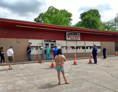 A group of people waiting outside Bear's Restaurant, with a sign indicating it's open, and traffic cones in front.