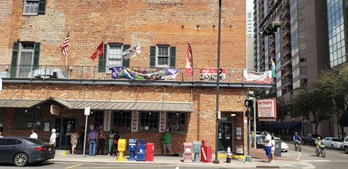 A brick building with flags and banners, people outside, and a street with cyclists and pedestrians.