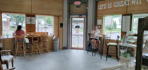 A cozy café interior with wooden walls, two customers sitting at tables, and a welcoming entrance.
