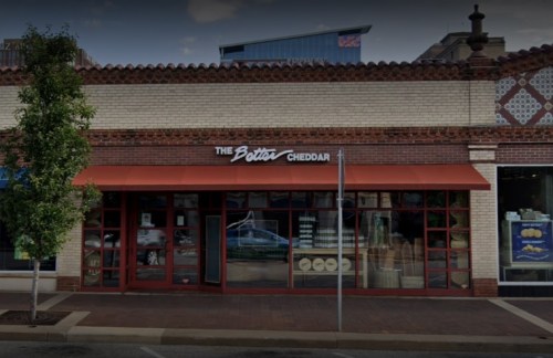 Exterior of a store named "The Better Cheddar," featuring large windows and an orange awning.