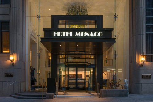 Entrance of Hotel Monaco featuring modern glass doors and a stylish sign, illuminated at night.
