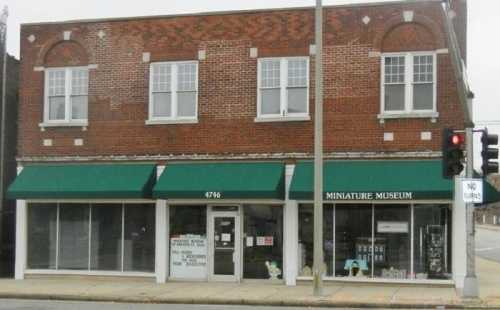 A brick building with green awnings, featuring a sign for a Miniature Museum and large windows.