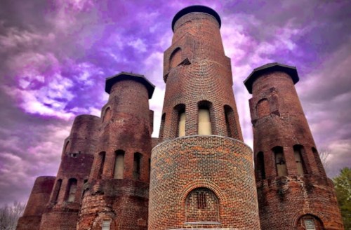 A dramatic view of a brick castle with four towers under a purple-tinged cloudy sky.