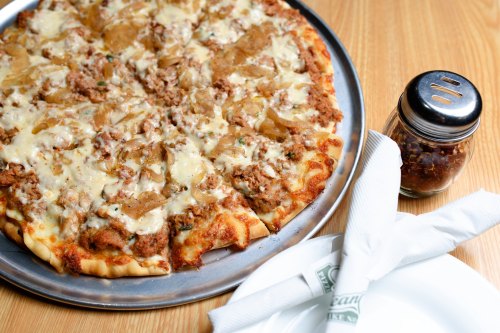 A large pizza topped with ground meat and pineapple, served on a metal tray with a shaker of seasoning nearby.