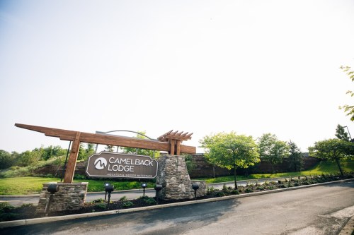 Sign for Camelback Lodge, featuring stone and wood design, surrounded by greenery and a clear sky.