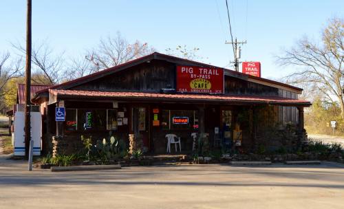 A rustic café with a wooden exterior and a red roof, featuring a sign that reads "Pig Trail Café" and outdoor seating.