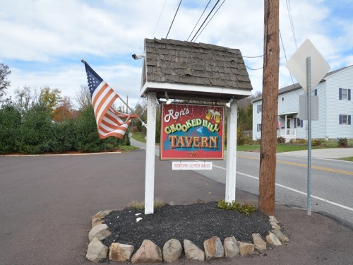Sign for Ron's Crooked Hill Tavern with an American flag, located at a roadside intersection.