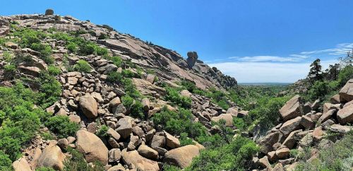A panoramic view of rocky hills and lush greenery under a clear blue sky.
