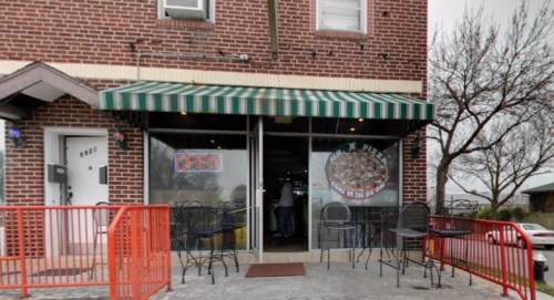 A small restaurant with a green and white striped awning, featuring outdoor seating and an "Open" sign in the window.