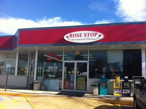 Exterior of Rose Stop, an international delicacy store, featuring a red and white sign and large glass windows.